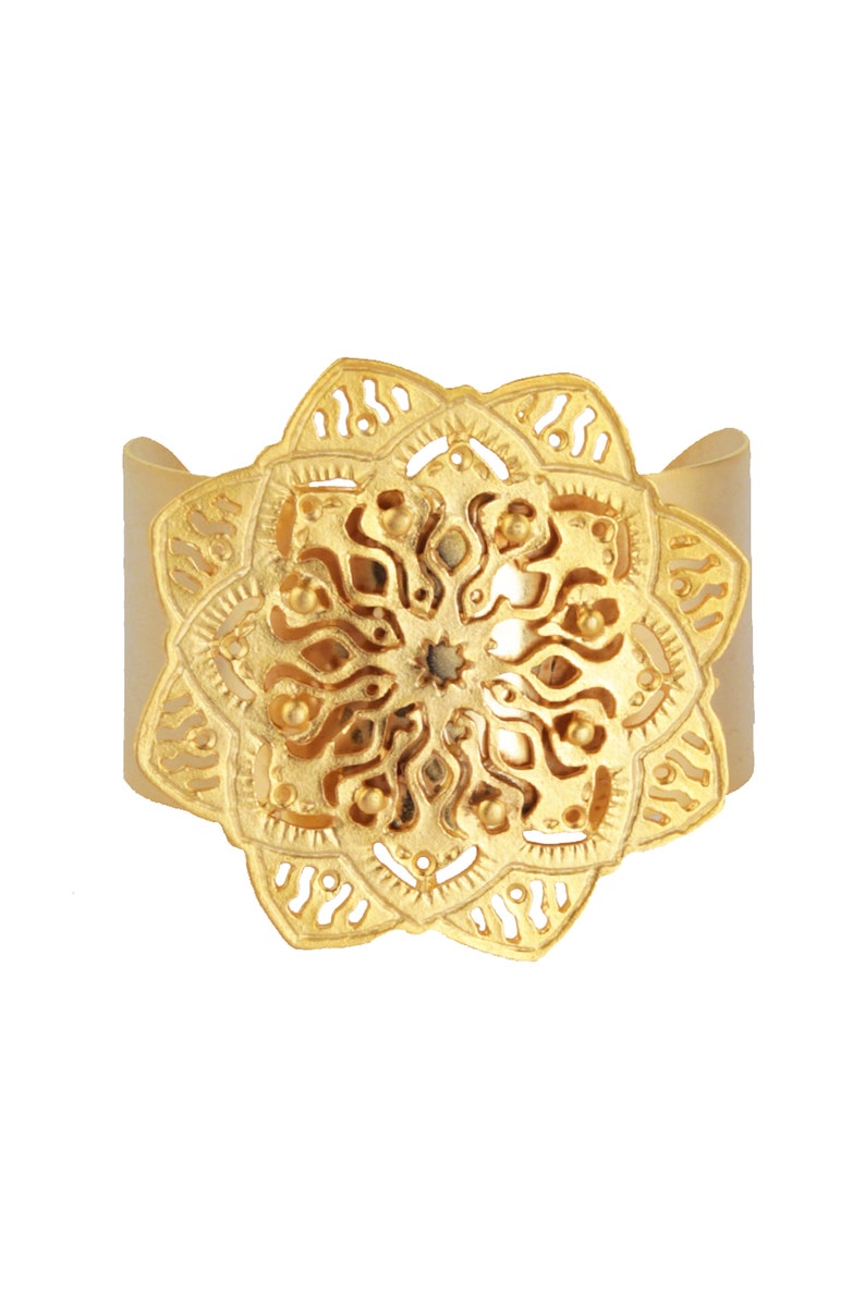 May include: Gold-toned metal cuff bracelet with a large, ornate, circular mandala design.