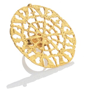 May include: A gold-toned ring with a large, circular, openwork design. The design features a repeating pattern of stylized leaves and swirls.