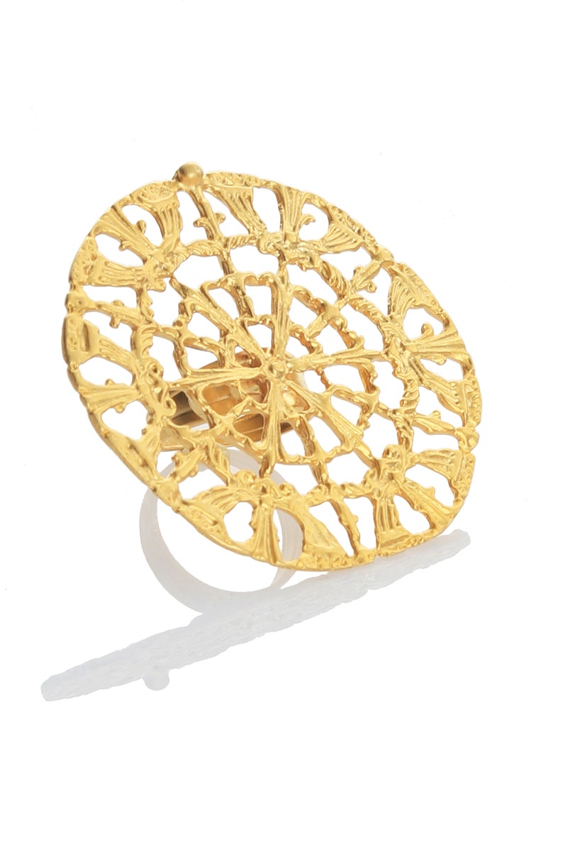 May include: A gold-toned ring with a large, circular, openwork design. The design features a repeating pattern of stylized leaves and swirls.