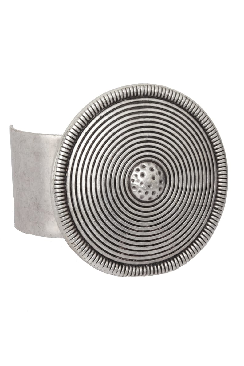 May include: A silver cuff bracelet with a large, round, concentric circle design. The center of the circle has a textured, raised dot.