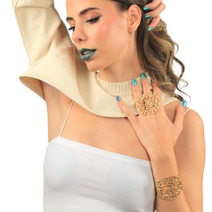 May include: A woman wearing a white crop top with a gold ring and bracelet. She is wearing a cream colored sweater over her shoulders and has teal nail polish.