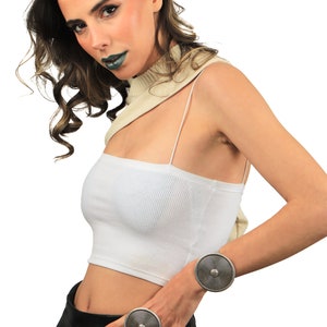 May include: A woman wearing a white crop top, black leather pants, and two silver rings with a circular design. The rings are on her wrist and finger.