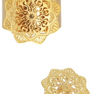 May include: A gold-toned ring with a large, intricate mandala design. The ring is wide and has a flat band.
