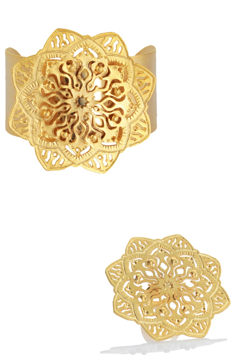May include: A gold-toned ring with a large, intricate mandala design. The ring is wide and has a flat band.