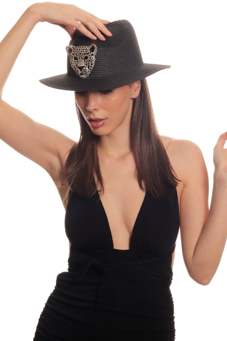 Puede incluir: Una mujer con un traje de ba&ntilde;o negro con un escote pronunciado y un sombrero negro de ala ancha con un dise&ntilde;o de leopardo con joyas.