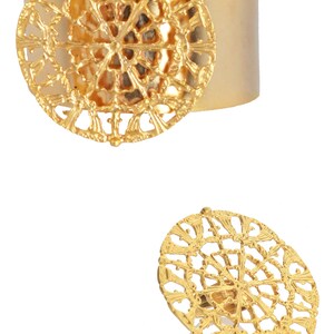 May include: A gold-toned metal ring with a large, intricate, circular design. The ring is open and adjustable.