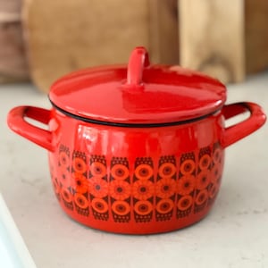 May include: Red enamel pot with a lid and two handles. The pot has a geometric pattern in black, orange, and red.