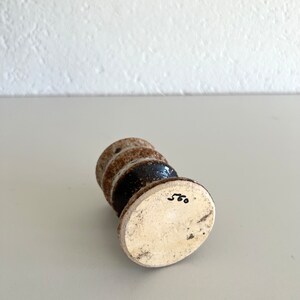 Pu&ograve; includere: Un piccolo vaso in ceramica bianca con una glassa marrone e una fascia nera attorno al centro. Il vaso ha una base rotonda e un corpo cilindrico. Il fondo del vaso &egrave; contrassegnato dal numero "560".