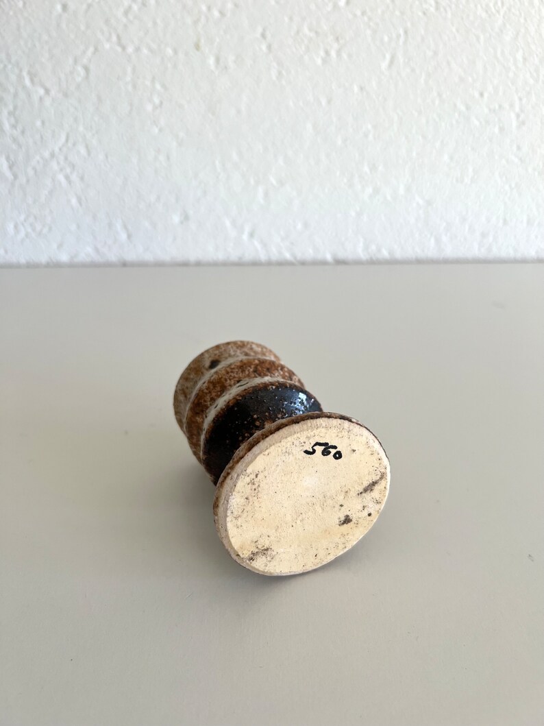 Pu&ograve; includere: Un piccolo vaso in ceramica bianca con una glassa marrone e una fascia nera attorno al centro. Il vaso ha una base rotonda e un corpo cilindrico. Il fondo del vaso &egrave; contrassegnato dal numero "560".