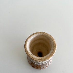 Pu&ograve; includere: Un piccolo vaso in ceramica bianca con una superficie ruvida e testurizzata. Il vaso ha un'ampia apertura rotonda e una base stretta.