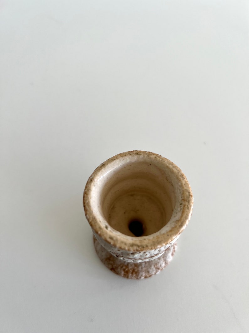 Pu&ograve; includere: Un piccolo vaso in ceramica bianca con una superficie ruvida e testurizzata. Il vaso ha un'ampia apertura rotonda e una base stretta.