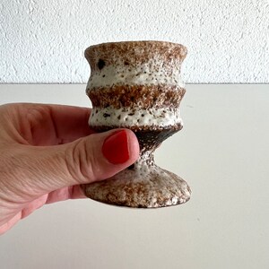 Pu&ograve; includere: Una piccola tazza in ceramica bianca e marrone con una superficie testurizzata e una base svasata. La tazza &egrave; perfetta per contenere piccoli oggetti come candele o ciondoli.