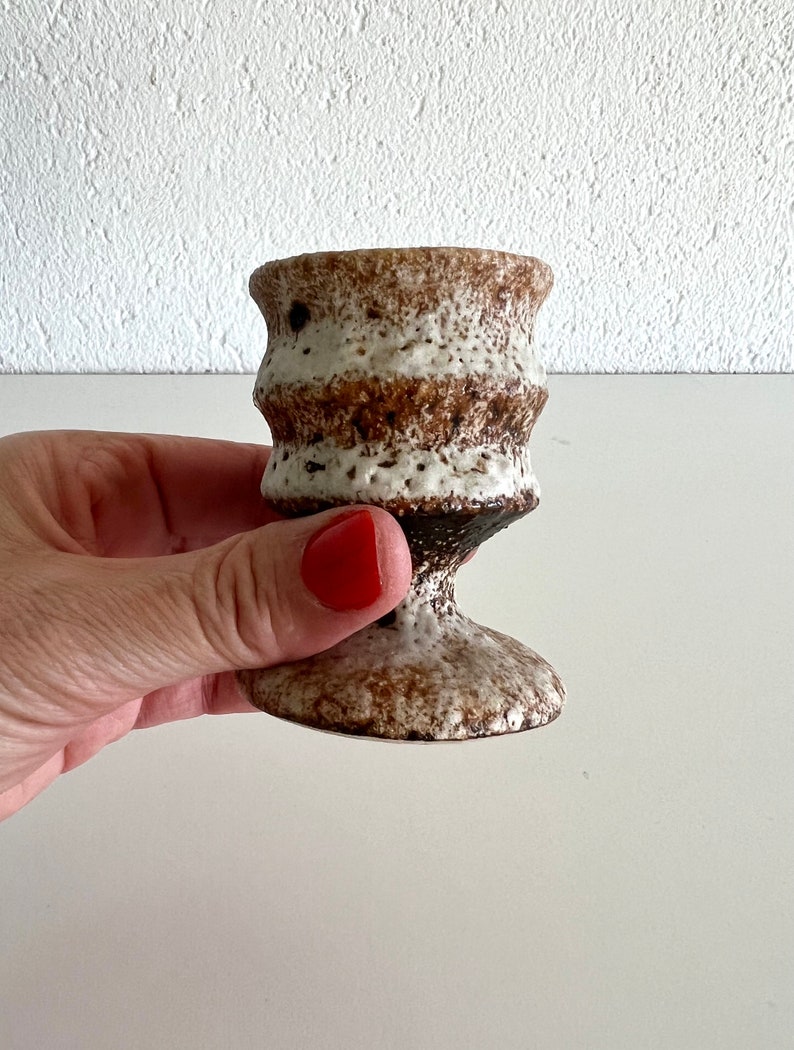 Pu&ograve; includere: Una piccola tazza in ceramica bianca e marrone con una superficie testurizzata e una base svasata. La tazza &egrave; perfetta per contenere piccoli oggetti come candele o ciondoli.