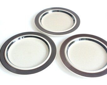 May include: Three white ceramic plates with brown and black trim. The plates are stacked on top of each other.