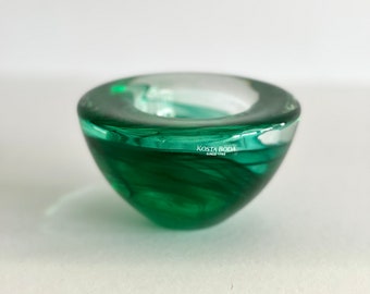 May include: A small, green glass candle holder with a swirl design. The holder is made by Kosta Boda, a Swedish glass company.
