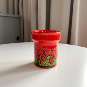 May include: Red ceramic flower pot with a white background. The pot has a tulip design with red tulips and green leaves.