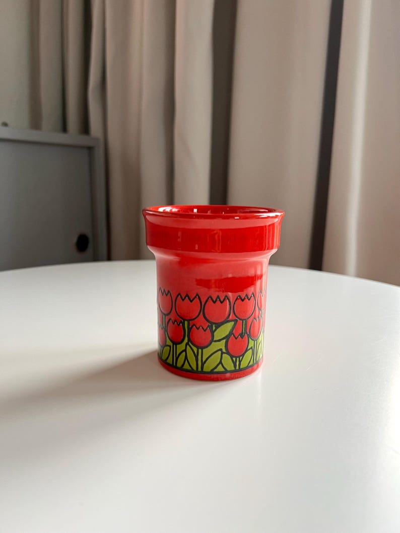 May include: Red ceramic flower pot with a white background. The pot has a tulip design with red tulips and green leaves.