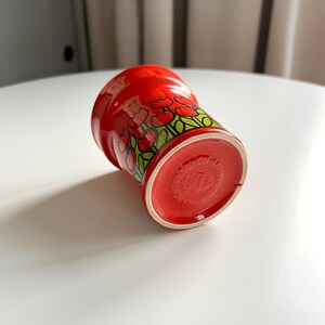 May include: Red ceramic mug with a floral design of red tulips and green leaves. The mug is turned upside down, showing the red bottom.