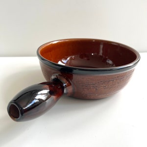 Op de afbeelding: Een bruine keramische fonduepot met een donkerbruine handgreep. De pot heeft een getextureerd oppervlak en een glanzende afwerking.