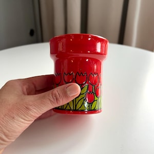 May include: Red ceramic cup with a black and green tulip design.