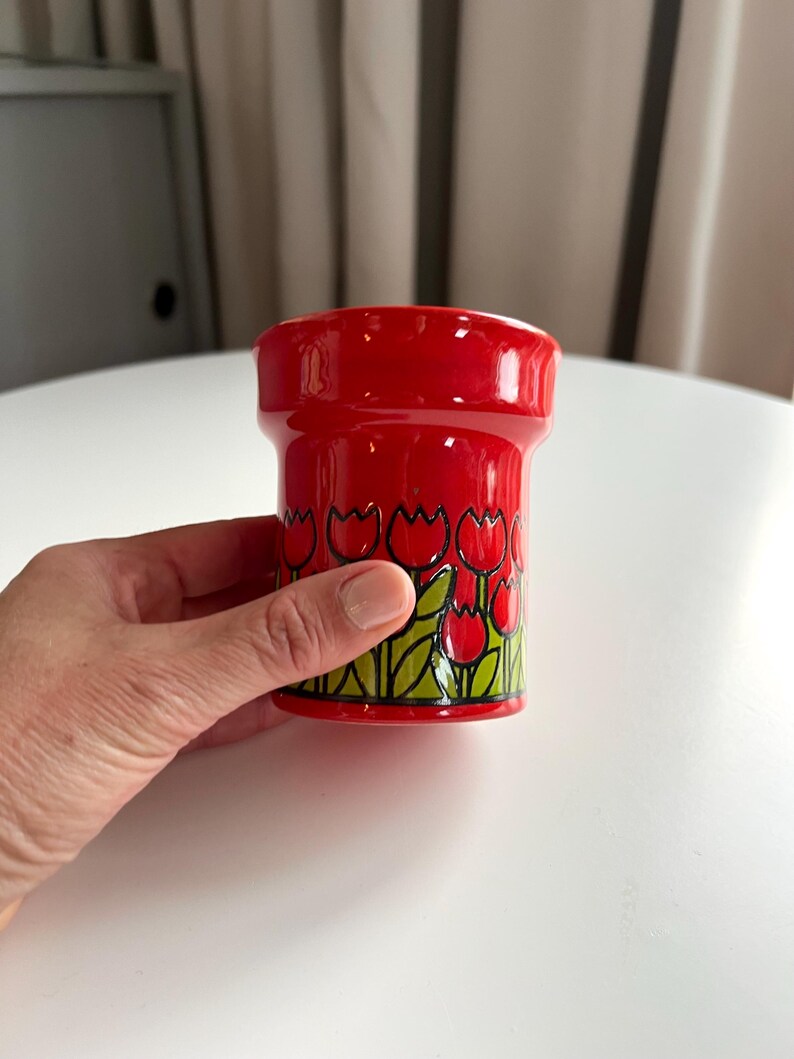 May include: Red ceramic cup with a black and green tulip design.
