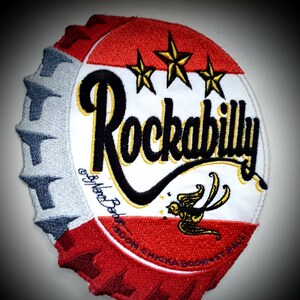 Könnte beinhalten: Roter, weißer und blauer gestickter Patch in Form einer Flaschenkappe mit dem Wort "Rockabilly" in schwarzen und goldenen Buchstaben. Drei goldene Sterne befinden sich über dem Wort. Ein kleiner Vogel ist in Gold auf der unteren Hälfte des Patches gestickt.