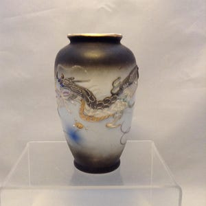 May include: A small, decorative vase with a black and white gradient. The vase features a detailed dragon design in silver and gold, with blue accents. The rim is gold. A unique piece for home decor.