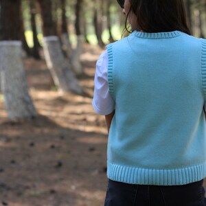 May include: A light blue knitted vest with a ribbed hem and a white t-shirt underneath.