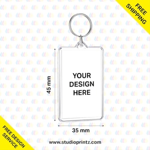 Op de afbeelding: Een transparante sleutelhanger van plastic met een zilveren metalen ring. De sleutelhanger heeft een rechthoekige ruimte voor een gepersonaliseerd ontwerp. De tekst "YOUR DESIGN HERE" is op de sleutelhanger gedrukt. De sleutelhanger is 4,5 cm breed en 4,5 cm hoog.