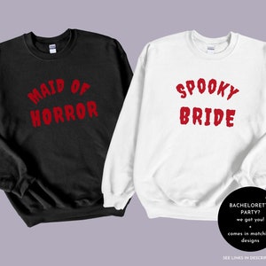 May include: Two black and white sweatshirts with red text. The black sweatshirt says "Maid of Horror" and the white sweatshirt says "Spooky Bride".