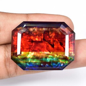 Könnte beinhalten: Ein großer, facettierter, irisierender Edelstein mit einem Regenbogen aus Farben, darunter Rot, Orange, Gelb, Grün, Blau und Lila. Der Edelstein ist in einer rechteckigen Form mit abgeschrägten Kanten geschliffen.