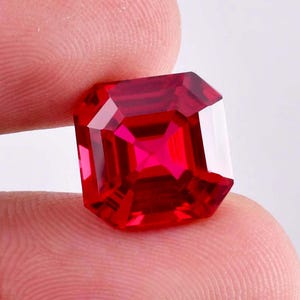 May include: A deep red gemstone with a square emerald cut.