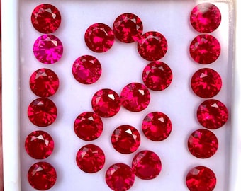 May include: A collection of 20 round, red gemstones in a white box. The gemstones are arranged in a pattern, with some forming the shape of a number eight.