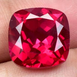 Peut inclure: Une pierre précieuse rouge foncé de taille coussin. La pierre précieuse est facetée et a un grand éclat.