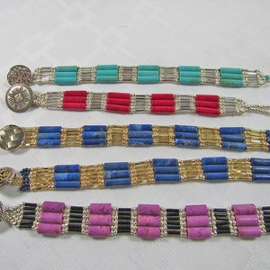 Puede incluir: Cinco pulseras de cuentas con cierres plateados. Las pulseras presentan cuentas de diferentes colores, incluyendo turquesa, rojo, azul, dorado y morado.