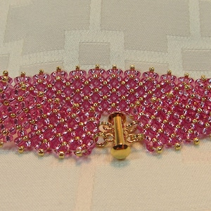 May include: A pink beaded bracelet with a gold clasp. The bracelet is made of small, round beads that are arranged in a pattern. The clasp is a simple, gold-toned design.