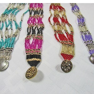 May include: Four beaded necklaces with different coloured beads and decorative metal accents. The necklaces are turquoise, pink, red, and purple.