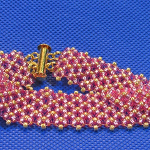 May include: A pink and gold beaded bracelet with a gold clasp. The bracelet is made of small, round beads that are arranged in a geometric pattern.