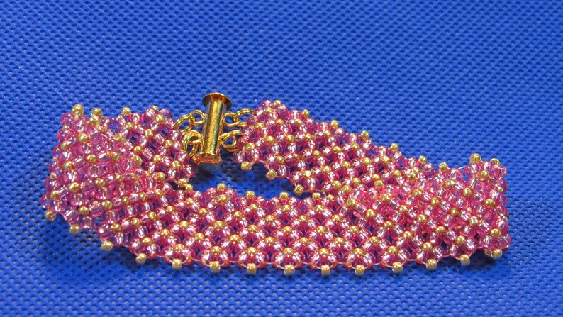 May include: A pink and gold beaded bracelet with a gold clasp. The bracelet is made of small, round beads that are arranged in a geometric pattern.