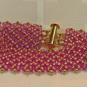 May include: A pink beaded bracelet with a gold clasp. The bracelet is made of small, round beads that are arranged in a pattern. The clasp is a simple, gold-toned toggle clasp.