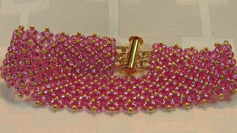 May include: A pink beaded bracelet with a gold clasp. The bracelet is made of small, round beads that are arranged in a pattern. The clasp is a simple, gold-toned toggle clasp.