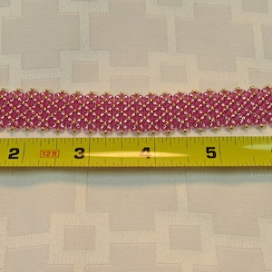 May include: Pink beaded bracelet with gold clasps, measured at 7 inches long.