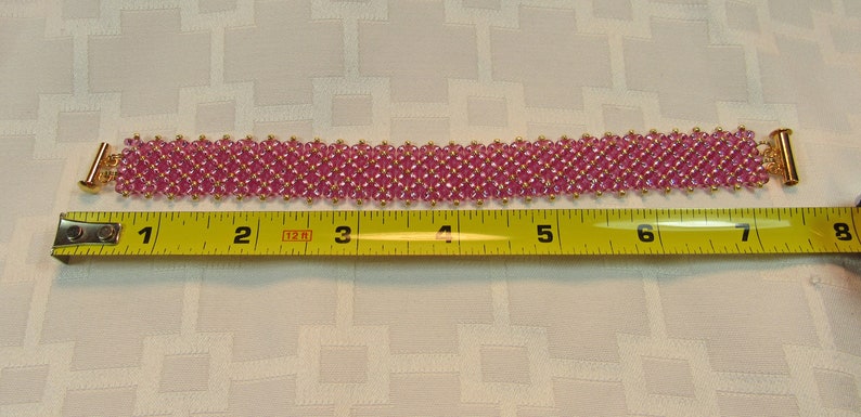 May include: Pink beaded bracelet with gold clasps, measured at 7 inches long.