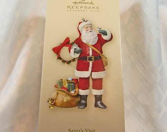 May include: A Hallmark Keepsake Ornament Club Christmas ornament featuring Santa Claus holding a bird in his hand. He is wearing a red suit with a white trim and a black belt. He is carrying a bag of gifts on his back. The ornament is titled "Santa's Visit" and is a Christmas decoration.