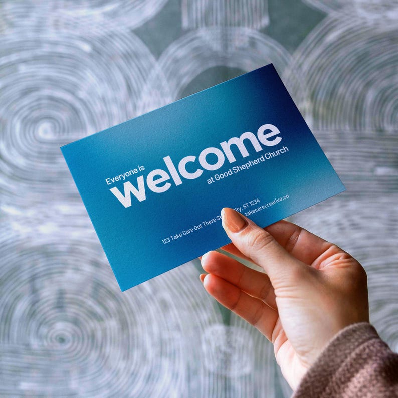 Pode incluir: Um cart&atilde;o de boas-vindas com gradiente azul com texto branco. O cart&atilde;o diz "Everyone is welcome at Good Shepherd Church". O texto adicional inclui um endere&ccedil;o e um site. O cart&atilde;o &eacute; segurado por uma pessoa.
