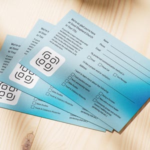 Pode incluir: Pilhas de cart&otilde;es azuis claros com um design gradiente. Cada cart&atilde;o tem um c&oacute;digo QR e campos de texto para nome, telefone e e-mail. Os cart&otilde;es s&atilde;o para a Good Shepherd Church.