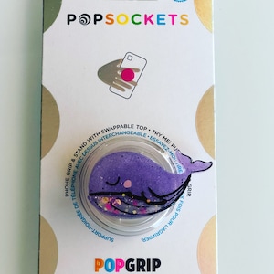 May include: A purple whale PopSocket phone grip and stand with a clear base. The whale design has a glittery belly and black outline. The packaging reads "POPSOCKETS" and "POPGRIP".