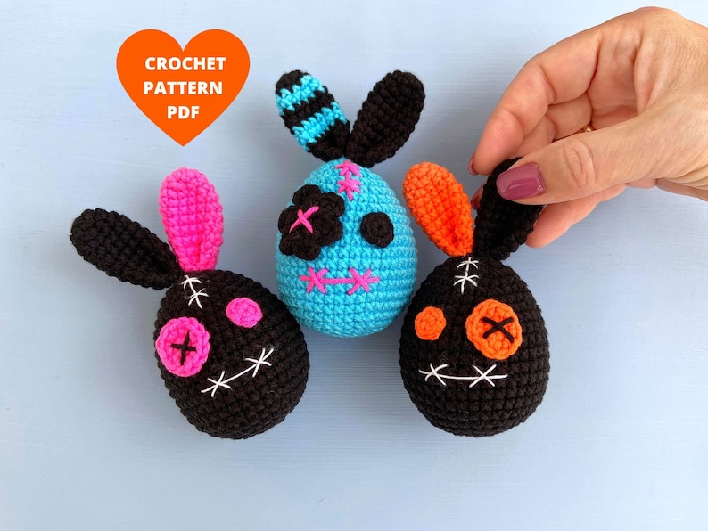 May include: Three crocheted Easter bunny ornaments with stitched-on eyes and mouths. The bunnies are black, blue, and orange.