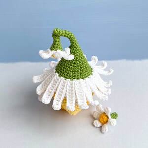 May include: A crocheted flower with a green stem and white petals. The flower has a yellow center and is sitting on a white surface.