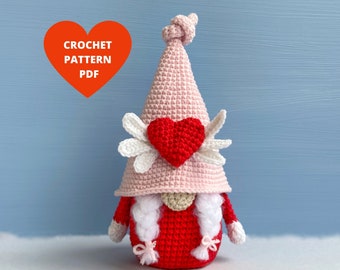 May include: Crochet pattern PDF for a Valentine's Day gnome with a pink hat, white wings, and a red heart. The gnome is wearing a red sweater and has white braids.